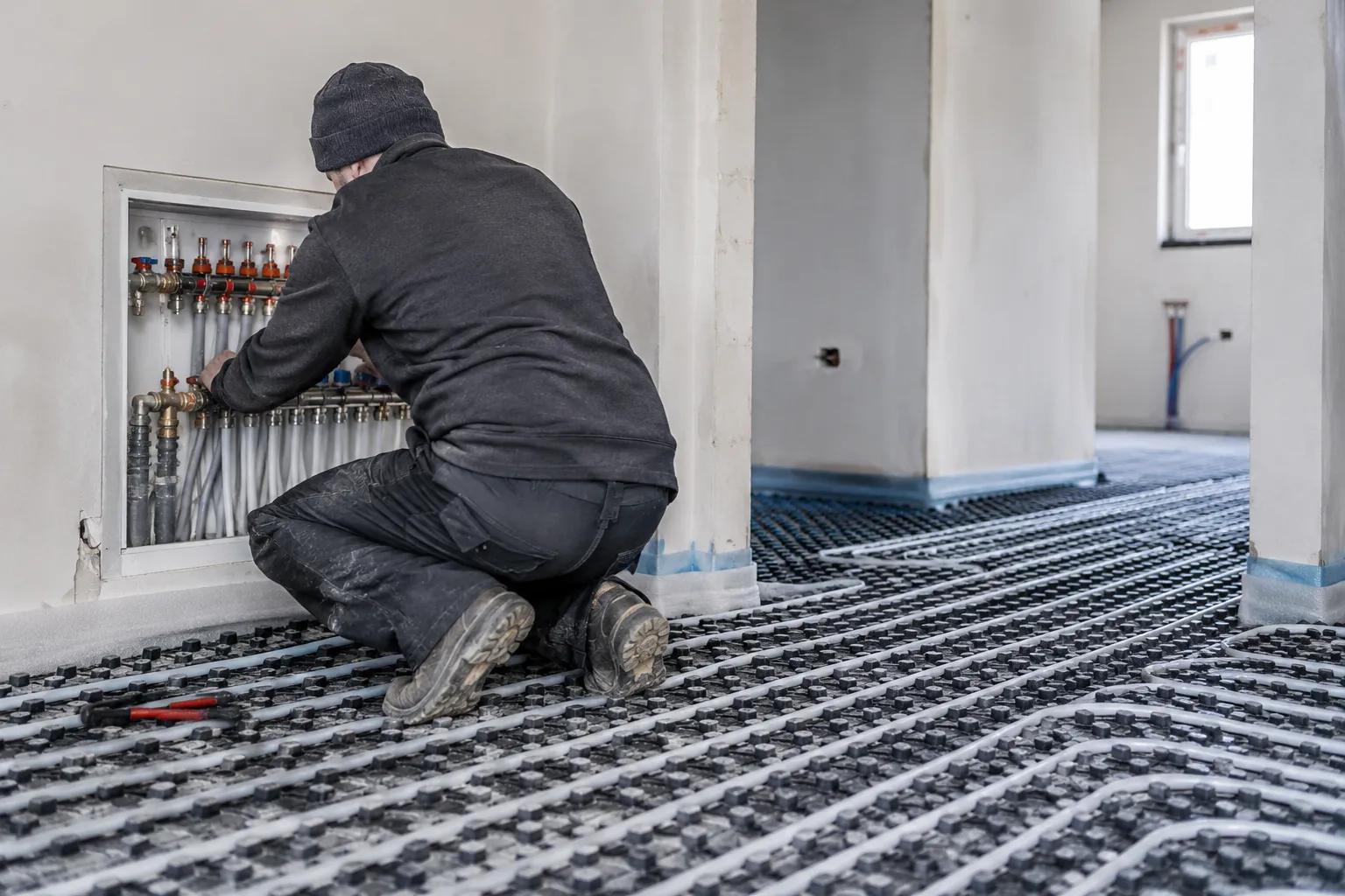 Instalator podczas pracy przy rozdzielaczu ogrzewania podłogowego w nowym domu.